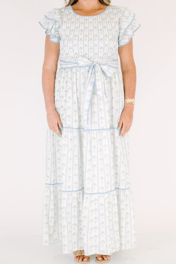 Chic Soul plus size clothing, white tiered dressed with a smocked texture on the chest flutter sleeves a bow that ties around the waist and a blue floral pattern throughout 