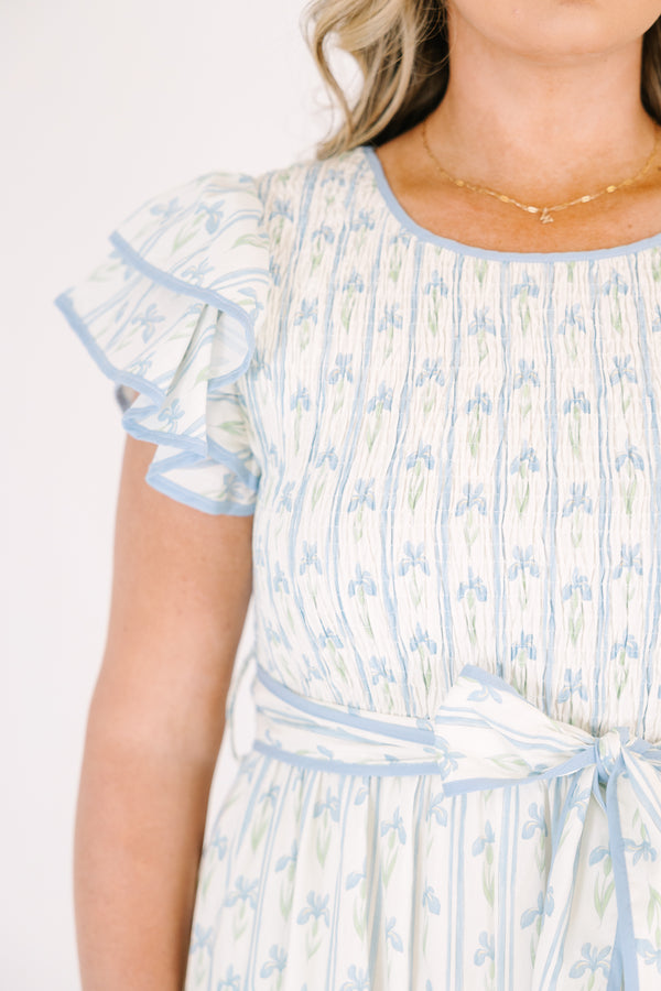 Chic Soul plus size clothing, white tiered dressed with a smocked texture on the chest flutter sleeves a bow that ties around the waist and a blue floral pattern throughout 