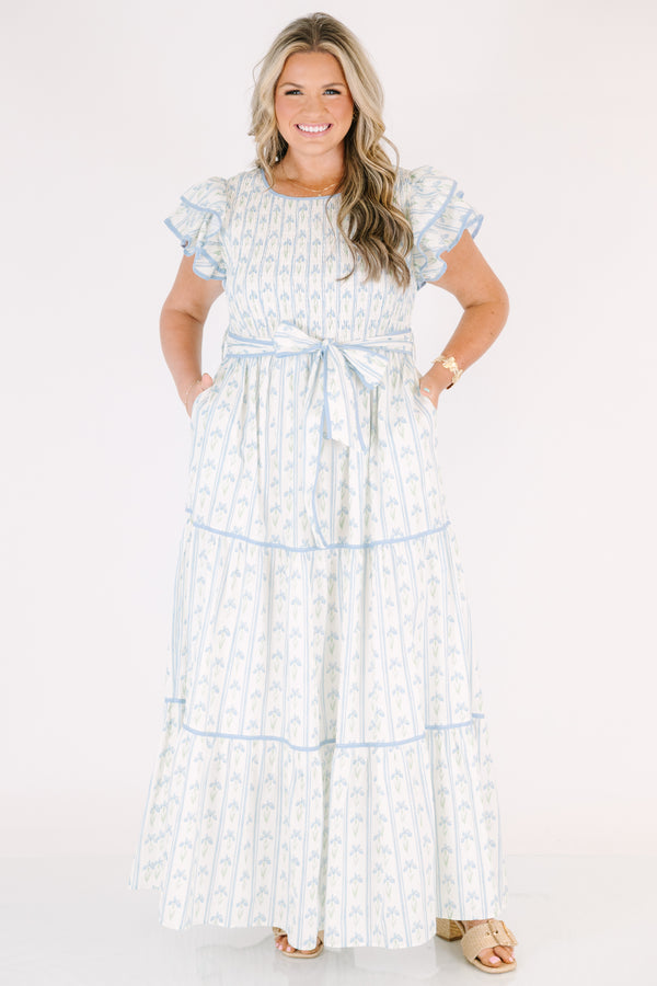 Chic Soul plus size clothing, white tiered dressed with a smocked texture on the chest flutter sleeves a bow that ties around the waist and a blue floral pattern throughout 