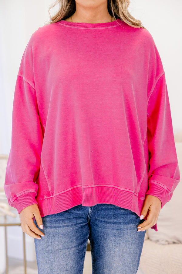 Person wearing a bright pink sweatshirt and blue jeans indoors.