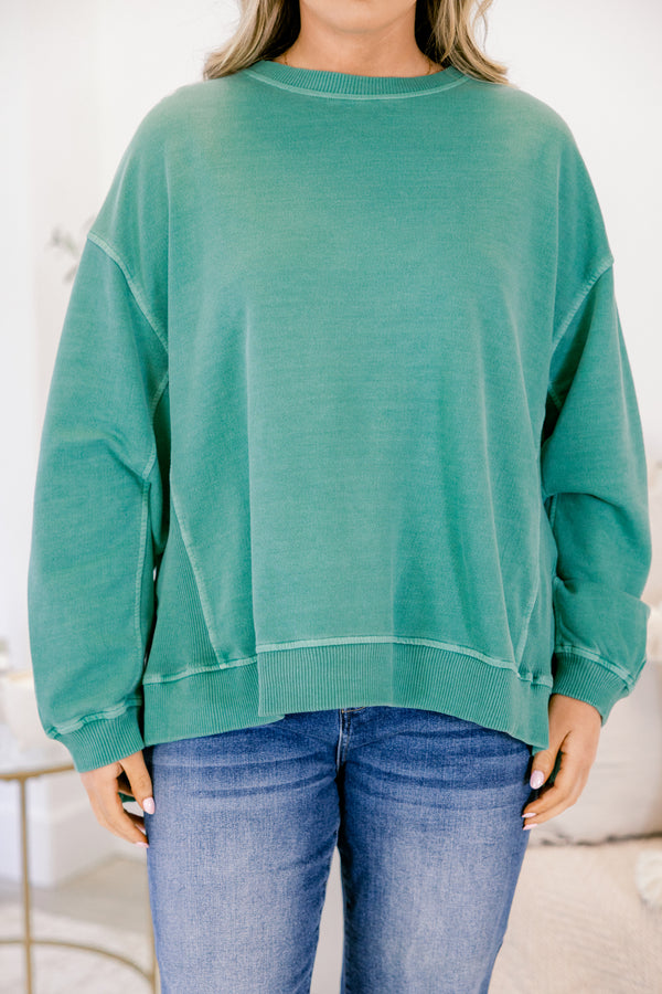 Person wearing a teal sweatshirt and blue jeans on a white background
