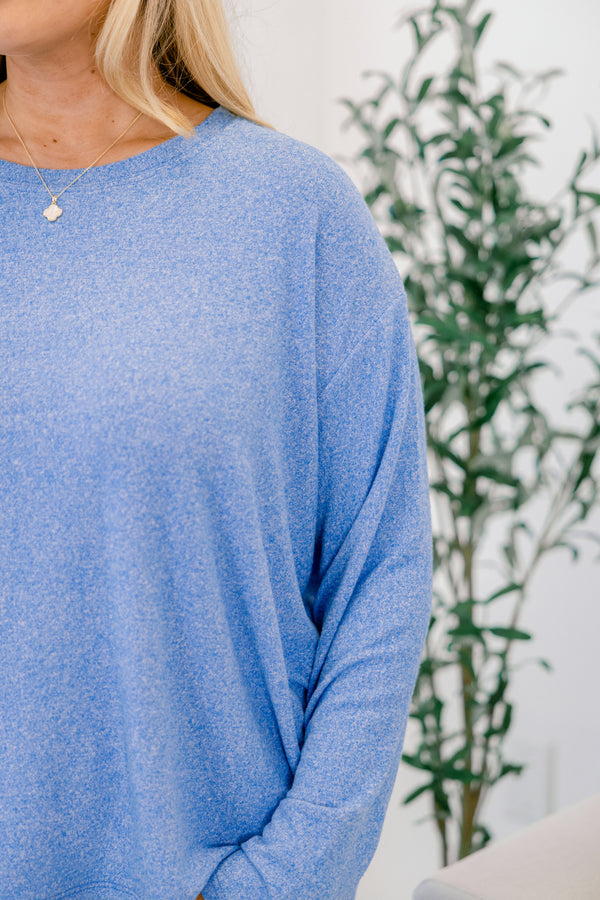 Person wearing a blue sweater with a plant in the background