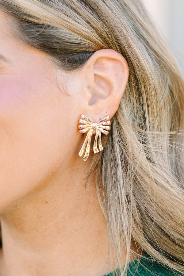 Plus Size gold bow-shaped stud earrings with a ribbed texture and dangling ribbon tails.