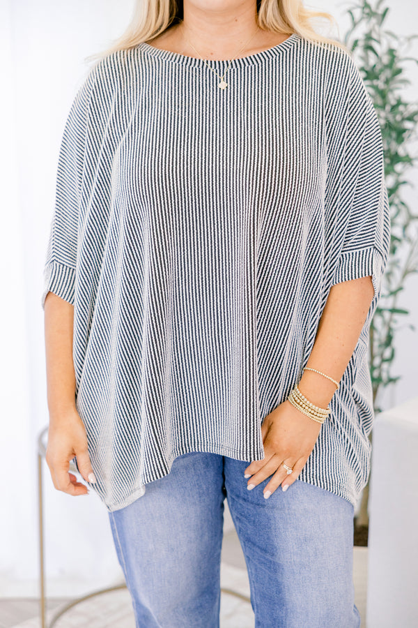 Woman wearing a black and white striped top and blue jeans indoors.
