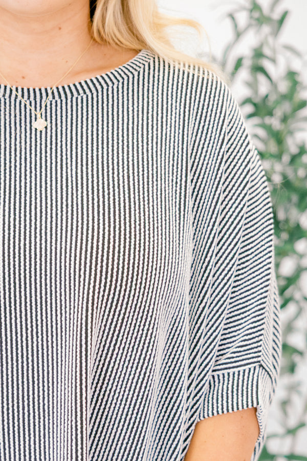 Person wearing a black and white striped shirt with a blurred green plant background