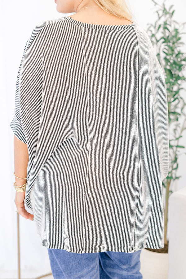 Person wearing a black and white striped poncho with blue pants indoors.