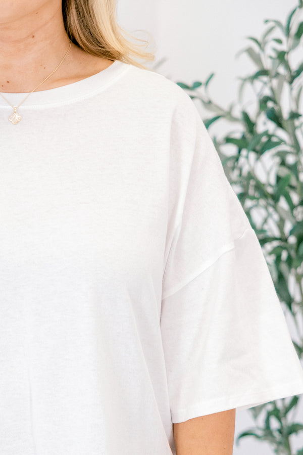 White t-shirt worn by a person with a blurred green plant background