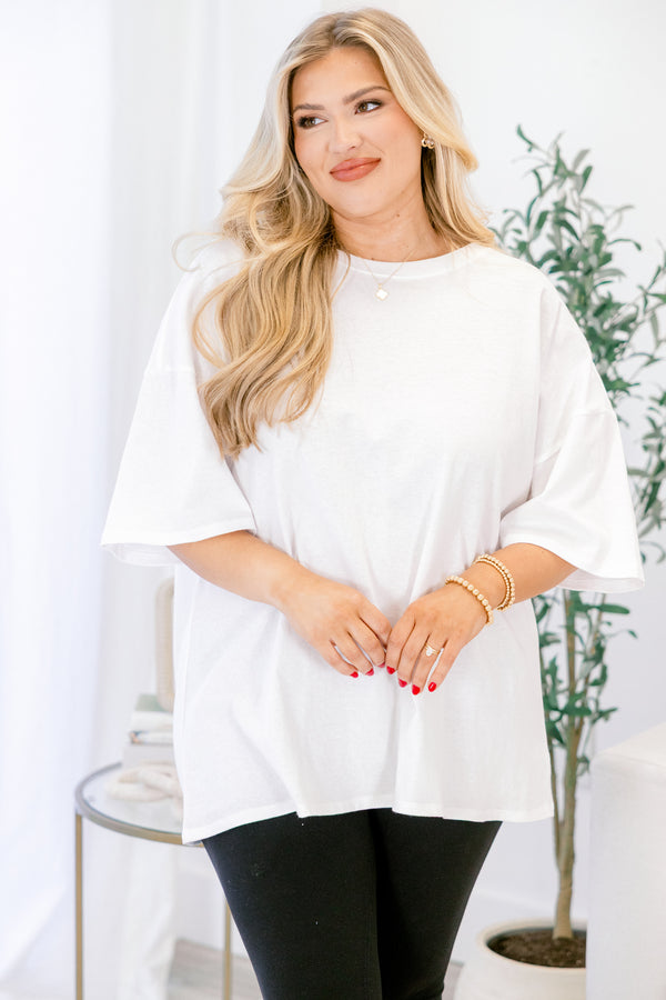 Woman wearing a white blouse and black pants in a bright room with a plant in the background