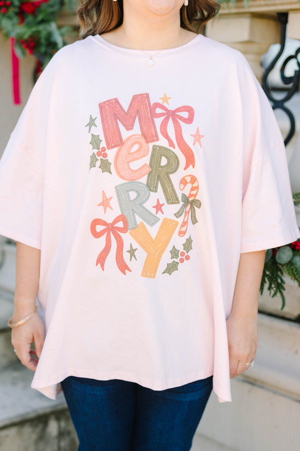 Plus size woman in a flowy cream pink boyfriend tee with a colorful 'MERRY' graphic and bows.