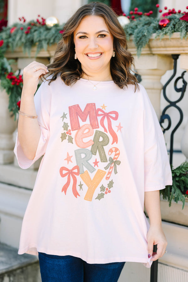 Plus size woman in a flowy cream pink boyfriend tee with a colorful 'MERRY' graphic and bows.