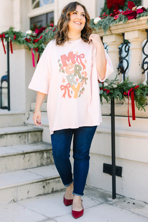 Plus size woman in a flowy cream pink boyfriend tee with a colorful 'MERRY' graphic and bows.
