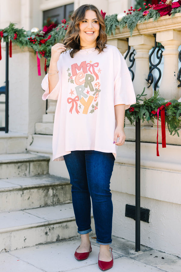 Plus size woman in a flowy cream pink boyfriend tee with a colorful 'MERRY' graphic and bows.