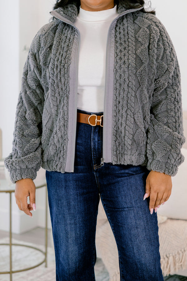 Person wearing a gray cable knit jacket over a white shirt and blue jeans.