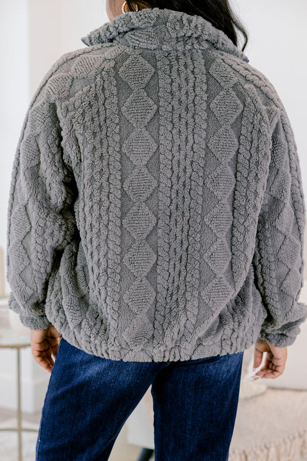 Person wearing a gray cable knit sweater with a blurred background