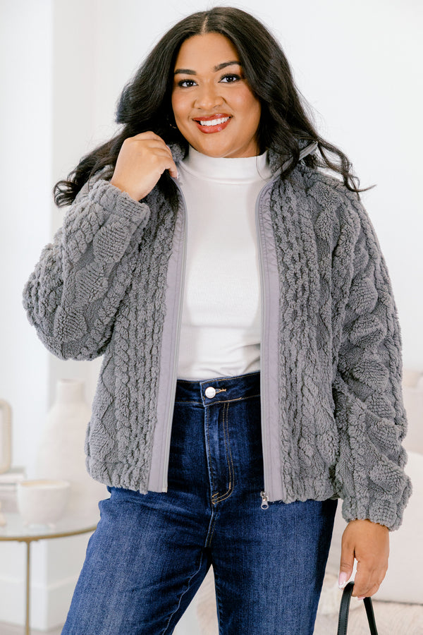 Woman wearing a gray cable knit cardigan over a white shirt and blue jeans.