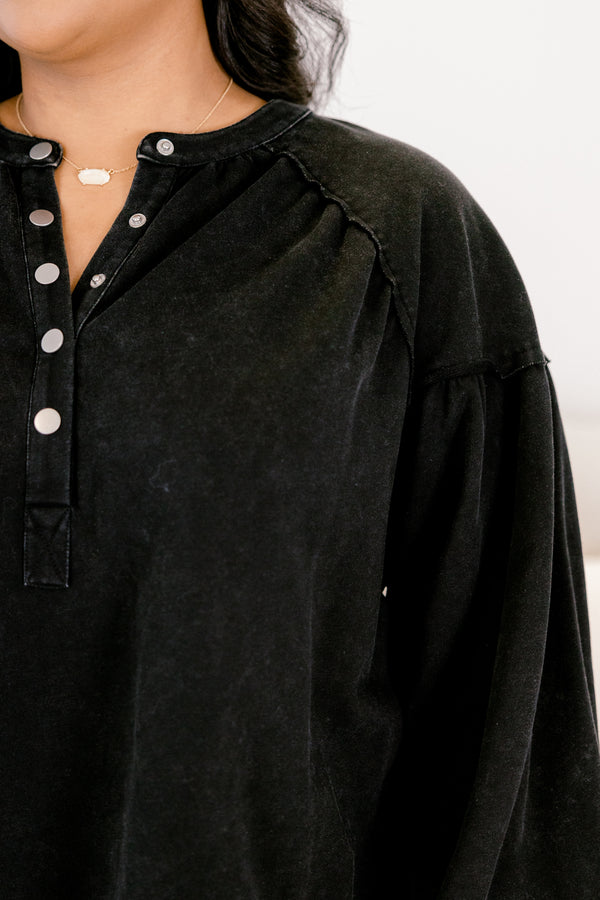 Black shirt with button details worn by a person, on a neutral background