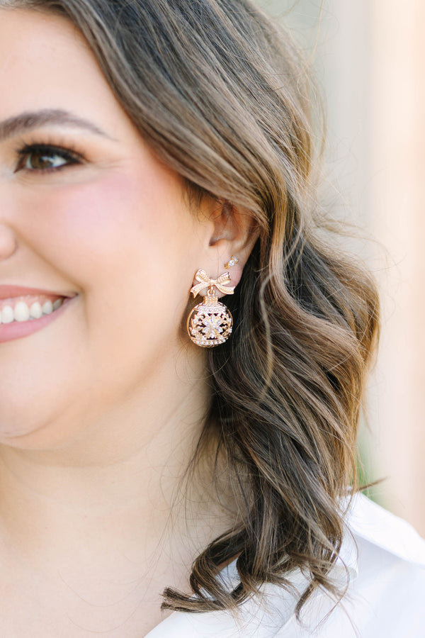 Gold crystal snowflake ornament earrings with a bow detail.