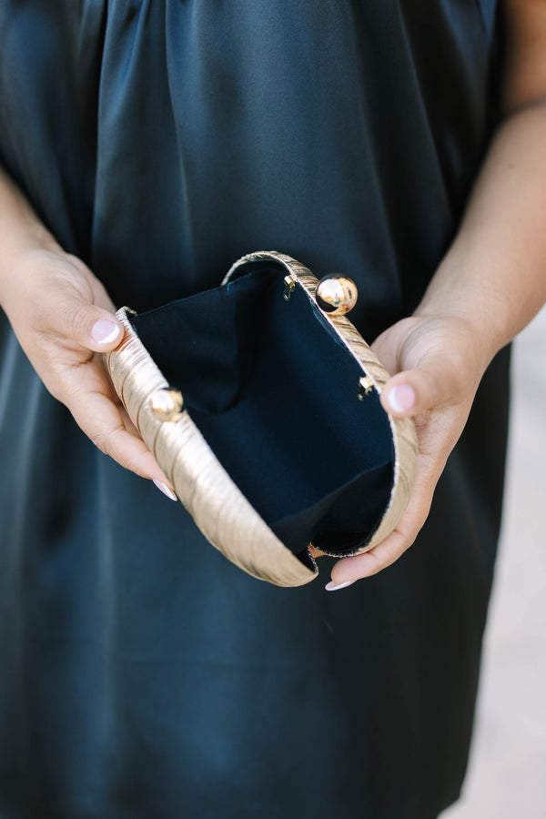 A woman holding a gold textured oval clutch with a gold chain strap and ball clasp.
