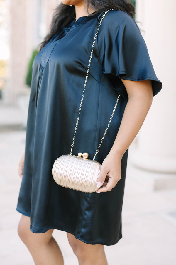 A woman holding a gold textured oval clutch with a gold chain strap and ball clasp.