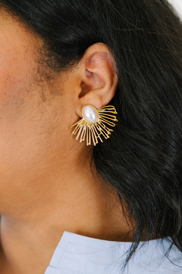 Plus Size gold sunburst earrings with a central oval white pearl on a light stone surface.