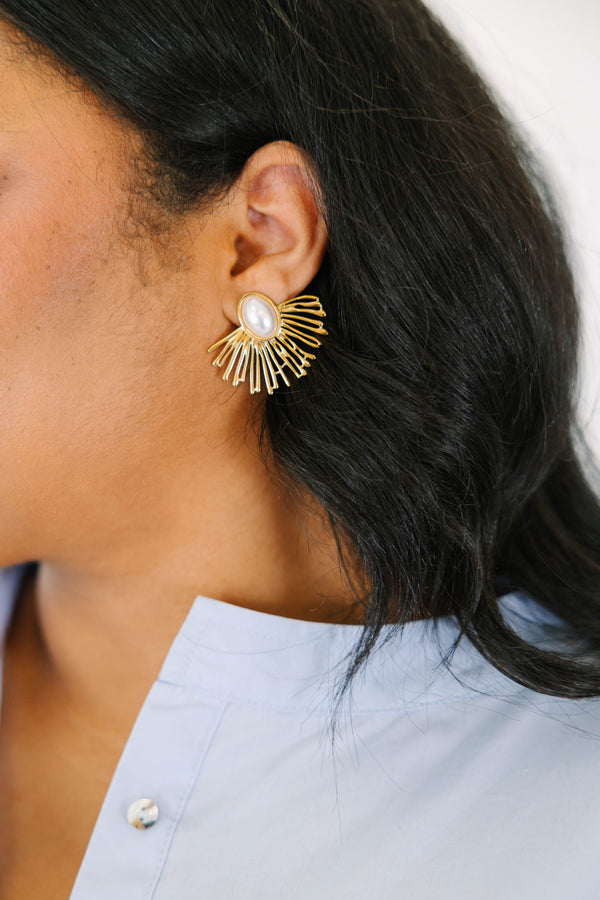 Plus Size gold sunburst earrings with a central oval white pearl on a light stone surface.