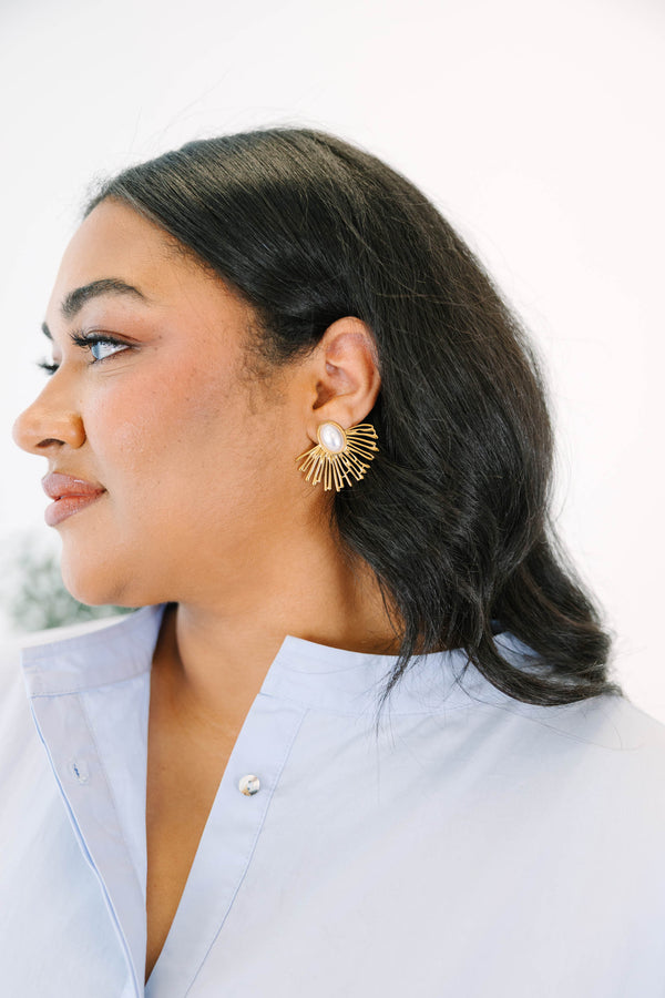 Plus Size gold sunburst earrings with a central oval white pearl on a light stone surface.