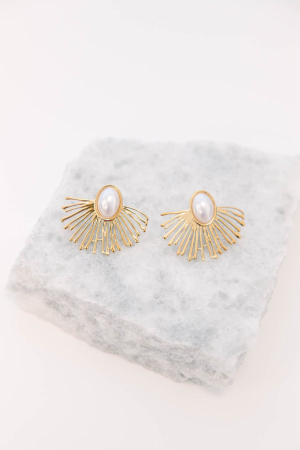 Plus Size gold sunburst earrings with a central oval white pearl on a light stone surface.