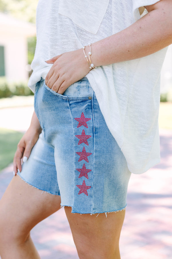 Plus Size medium wash high-rise denim shorts with red and blue rhinestone stars and raw hems.