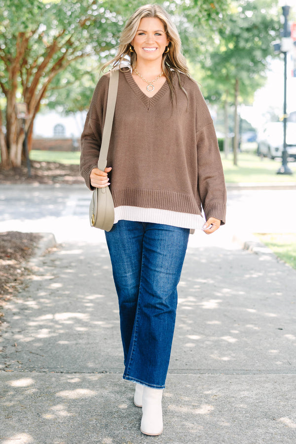 Plus size brown V-neck Sweater with a flowy fit and ribbed hem over blue jeans.