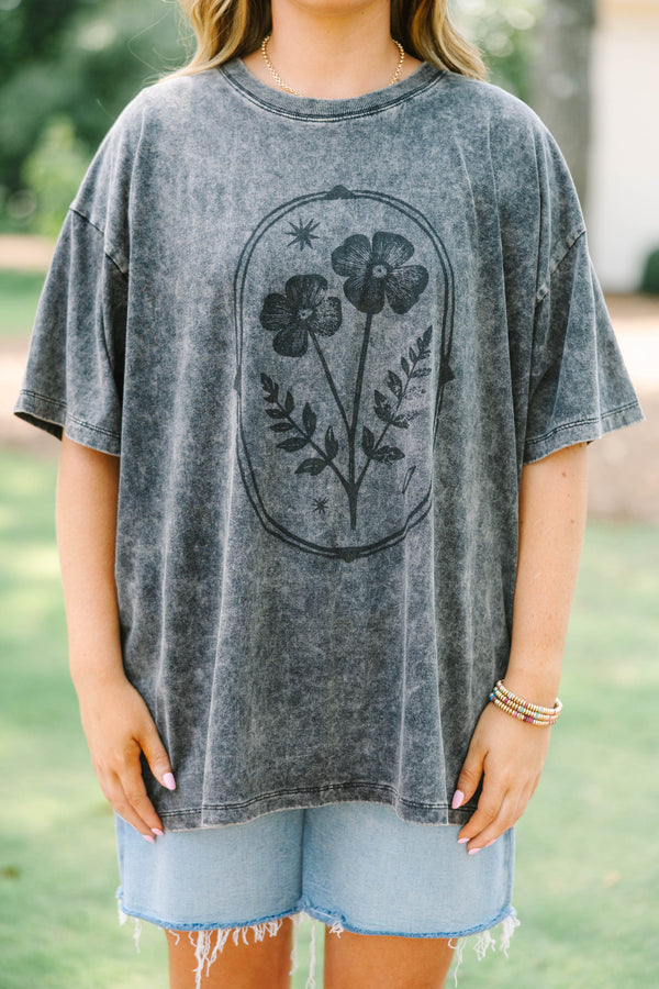 Plus size woman in a black acid wash relaxed tee with a floral graphic and light wash denim shorts.