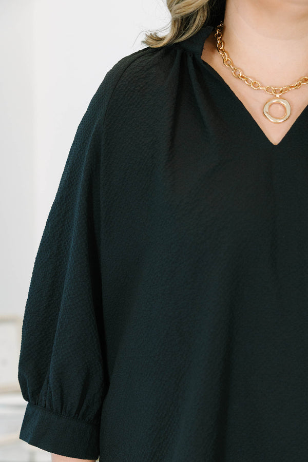 Plus size black top with a flowy fit, V-neckline, and textured polyester fabric.
