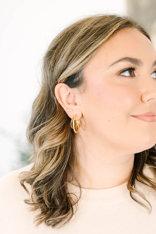 Plus Size gold triple hoop earrings and a small crystal stud on a woman's ear.