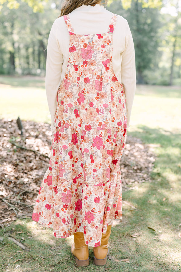 Plus Size pink floral tiered midi dress with overall straps over a white long-sleeve top.