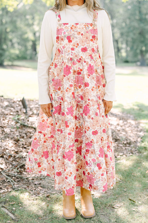 Plus Size pink floral tiered midi dress with overall straps over a white long-sleeve top.