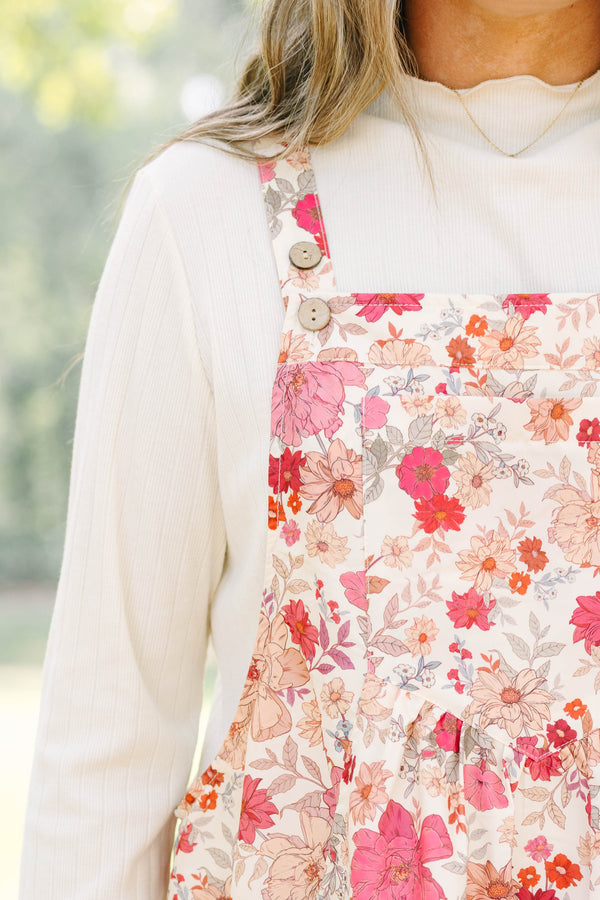 Plus Size pink floral tiered midi dress with overall straps over a white long-sleeve top.