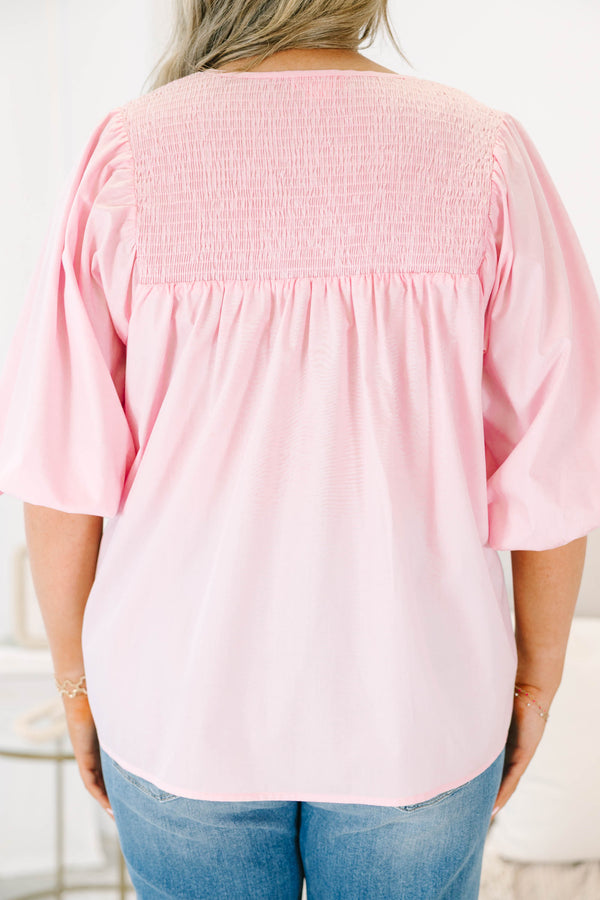 Plus size woman in a flowy pink top with smocked yoke detailing and short puff sleeves.