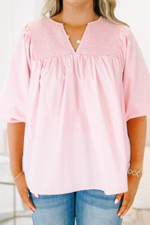 Plus size woman in a flowy pink top with smocked yoke detailing and short puff sleeves.