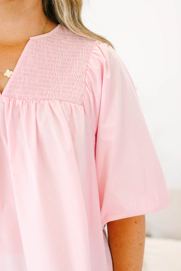 Plus size woman in a flowy pink top with smocked yoke detailing and short puff sleeves.