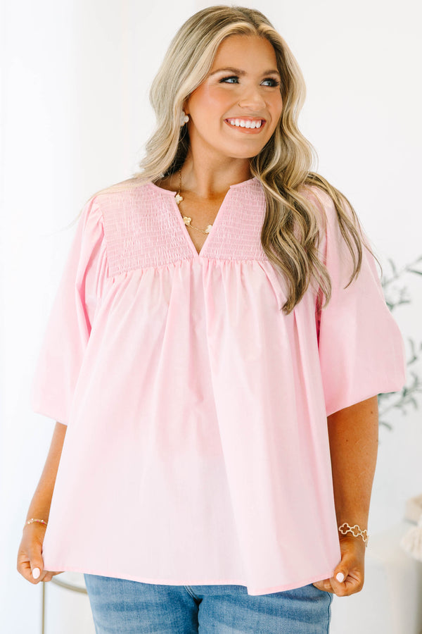 Plus size woman in a flowy pink top with smocked yoke detailing and short puff sleeves.