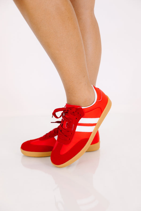 Red low-top sneakers with white side stripes and gum rubber soles.
