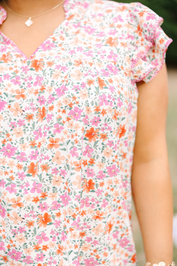 Chic Soul plus size clothing, pink top with a multi-color floral pattern throughout and fluttersleeeves with a slight v-neckline and ruffle details going along the collar of the top 
