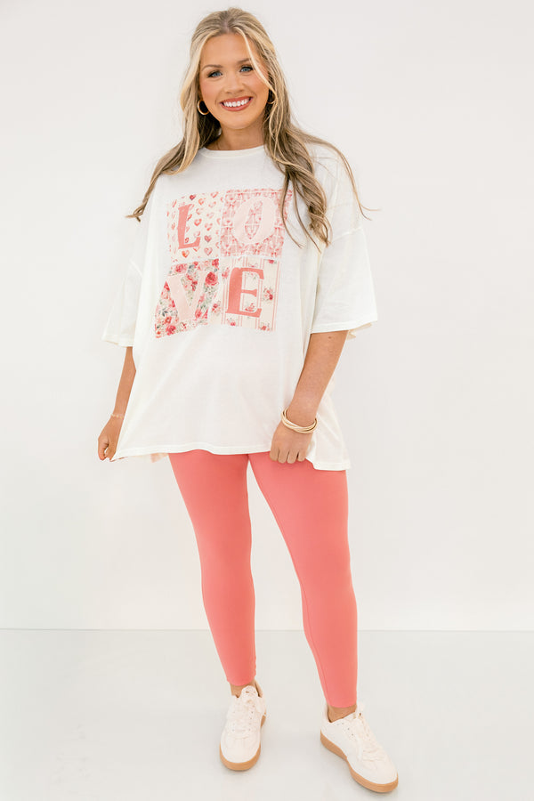 Woman wearing a white oversized t-shirt with floral text design and pink leggings on a white background