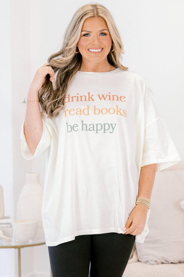 Woman wearing a white oversized t-shirt with text, sitting on a couch.