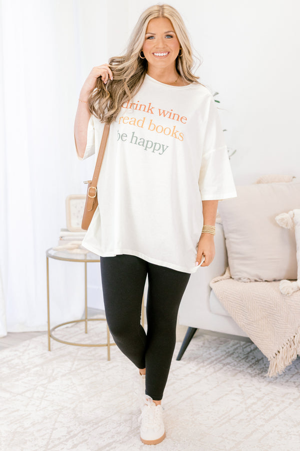 Woman wearing a white t-shirt with text, black leggings, and white sneakers in a living room.