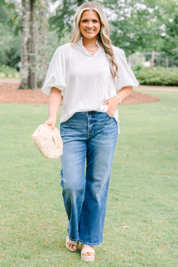 Plus Size ivory top with a ruffled v-neckline and short puff sleeves paired with blue jeans.