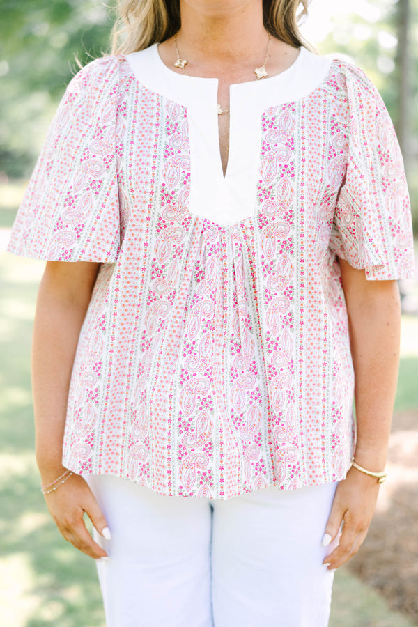 Plus Size pink paisley top with a white V-neckline, short flutter sleeves, and white pants.