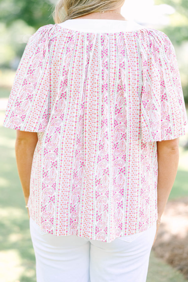 Plus Size pink paisley top with a white V-neckline, short flutter sleeves, and white pants.