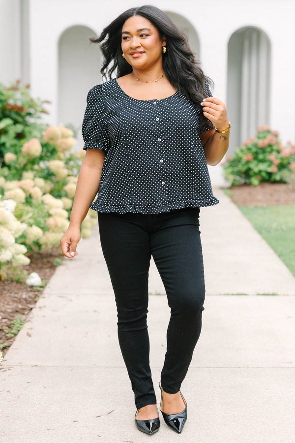 Short-sleeve black and white polka-dot blouse featuring a scoop neckline, front button closure, and a playful ruffled hem