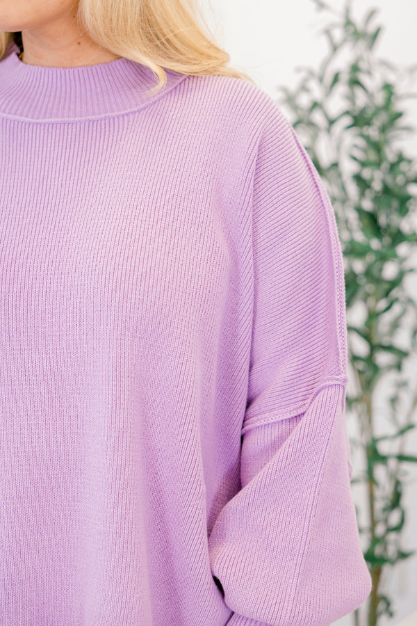 Person wearing a light purple sweater with a blurred green plant background