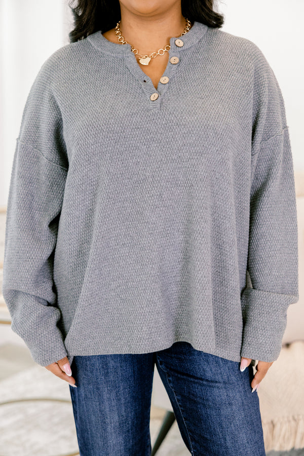 Person wearing a gray long-sleeve shirt with buttons and blue jeans against a neutral background